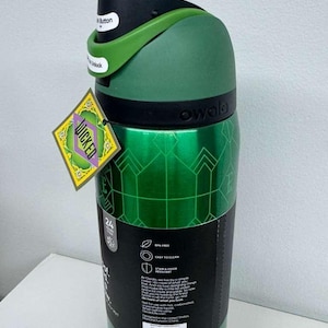 May include: A green Owala water bottle with a black lid and green handle. The bottle has a geometric pattern and a tag that says "WICKED". The lid has a button that says "Unlock".
