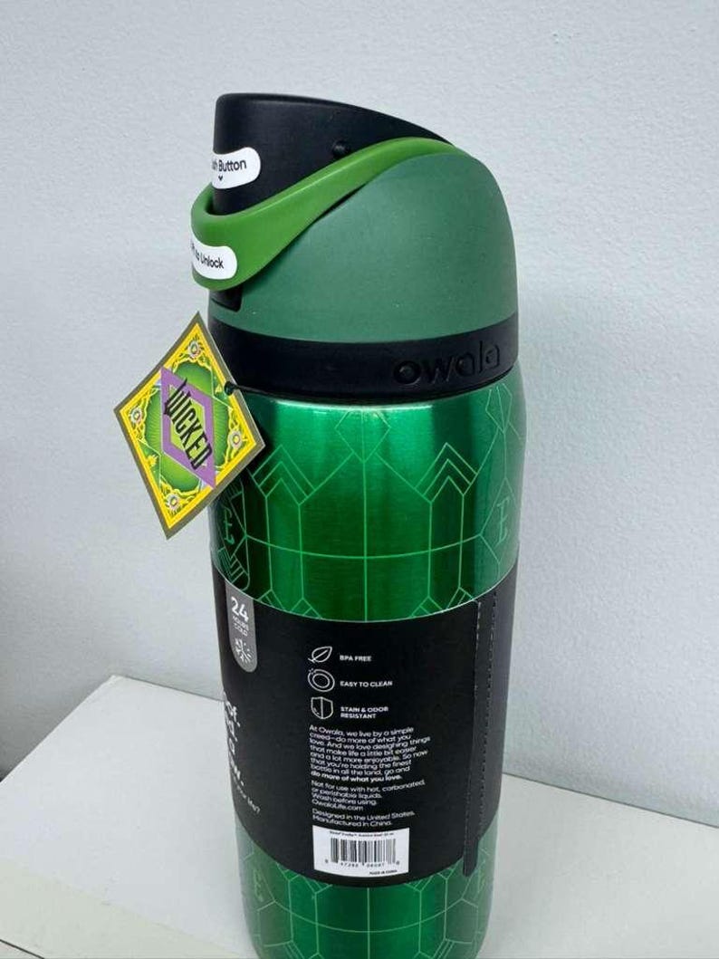 May include: A green Owala water bottle with a black lid and green handle. The bottle has a geometric pattern and a tag that says "WICKED". The lid has a button that says "Unlock".