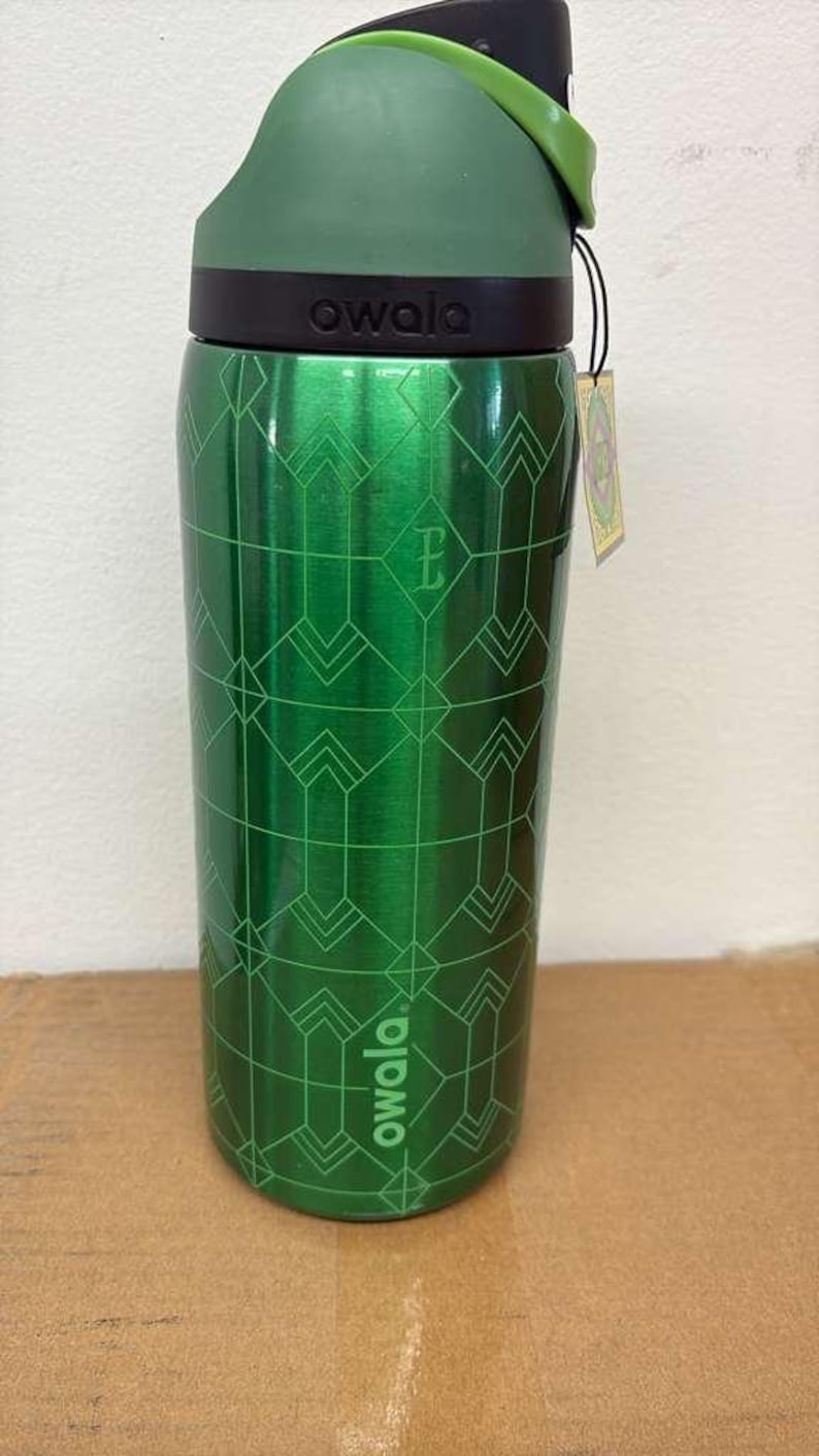 May include: Green Owala water bottle with a geometric pattern. The bottle has a green lid and a black band with the brand name. A small tag hangs from the bottle. The bottle is made of stainless steel.
