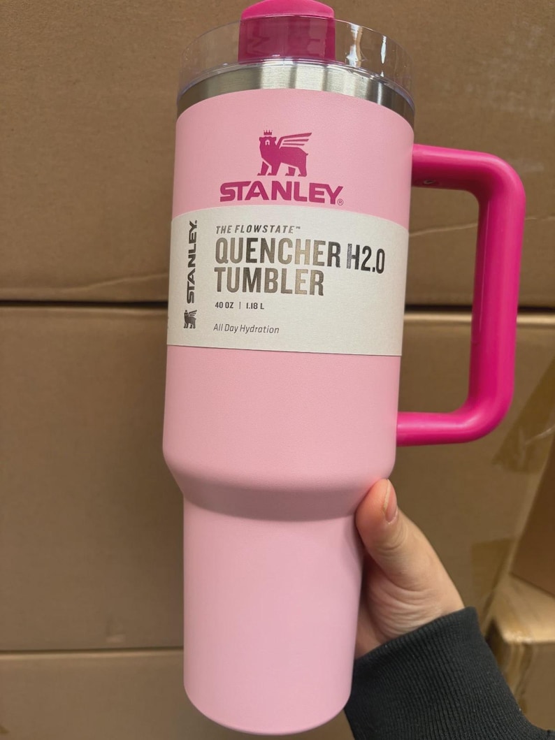 May include: A pink Stanley Quencher H2.0 tumbler with a matching handle and lid. The tumbler has the Stanley logo and product information printed on the front. It holds 1.18 L.