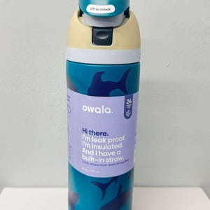 May include: A teal and cream-colored Owala water bottle with a shark pattern. The bottle has a built-in straw and is insulated. The text on the bottle says "Hi there. I'm leak proof. I'm insulated. And I have a built-in straw."