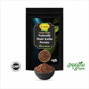 May include: A black pouch with the text "Premium Quality Naturally Made Katha Powder Pure Herbs" and a small bowl filled with brown powder. The image also includes the "Natural n Pure" logo and a "GMP" seal.
