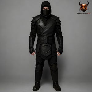 May include: A black ninja costume featuring a hood, face covering, and layered armour on the shoulders, arms, and legs. The costume includes a wide belt and gloves. The outfit is made of leather and is worn by a person.