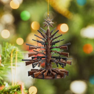 May include: A hanging Christmas tree ornament shaped like a tree trunk with various rifles and handguns extending from the sides as branches. The ornament features a star topper and is decorated with thin, colorful string lights throughout.