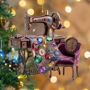 Könnte beinhalten: Ein bordeauxrotes Nähmaschinen-Ornament mit dem Namen NICOLE auf dem Arm. Es zeigt ein Stoffstück, das mit bunten, facettierten edelsteinartigen Formen, einem Schmetterling, einem Kompass und einem Baum verziert ist, sowie einen lila Stuhl.