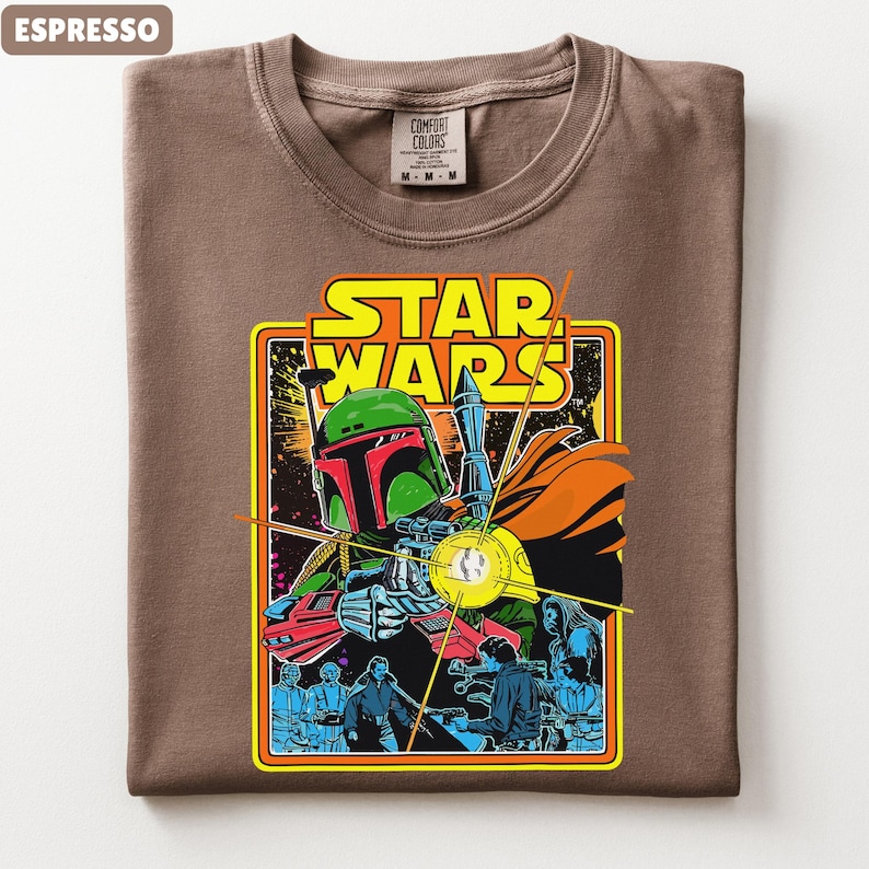 May include: Espresso-colored t-shirt featuring a Star Wars graphic. The graphic includes the words "STAR WARS" in yellow, and a colorful illustration of Boba Fett and other characters. The shirt is a Comfort Colors brand.