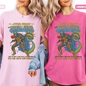 以下が含まれることがあります： 2枚のTシャツ。薄いピンクと濃いピンクで、それぞれスターウォーズのマンダロリアンのグラフィックが描かれています。「STAR WARS THE MANDALORIAN」の文字と「YOU ARE BOTH HUNTER PREY」のフレーズが含まれています。