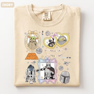Puede incluir: Camiseta de color marfil con personajes y gr&aacute;ficos de Star Wars. El dise&ntilde;o incluye im&aacute;genes de Grogu, el Mandaloriano y otros personajes, con el texto "THIS IS THE WAY".