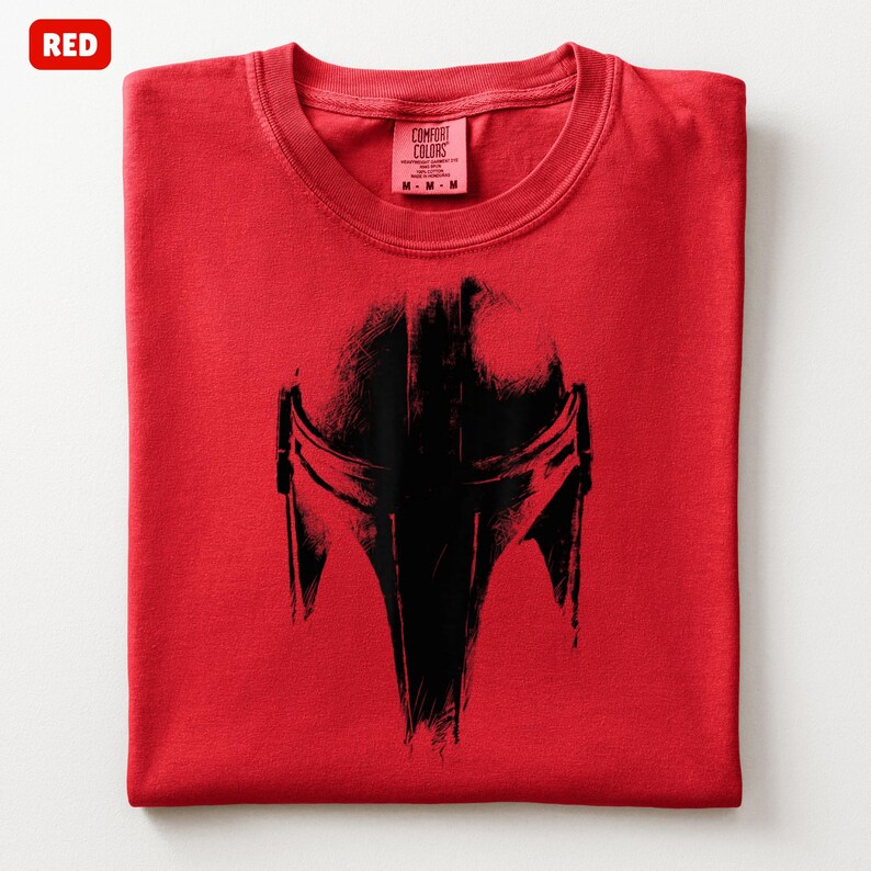 May include: A folded red t-shirt with a black helmet graphic. The shirt has a crew neck and a tag that reads "Comfort Colors". The word "RED" is in a red box in the upper left corner.