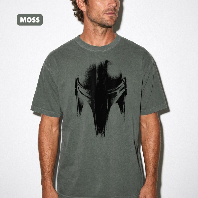 May include: A moss green t-shirt with a black helmet graphic. The shirt has a crew neck and short sleeves. The word "MOSS" is in a small rectangle in the upper left corner.