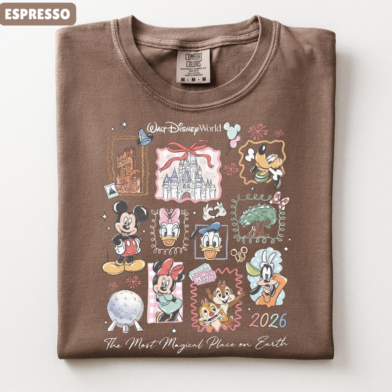 May include: Espresso-colored t-shirt featuring a colorful Disney World graphic. The design includes Mickey Mouse, Minnie Mouse, Donald Duck, and other characters, along with the text "2026" and "The Most Magical Place on Earth."