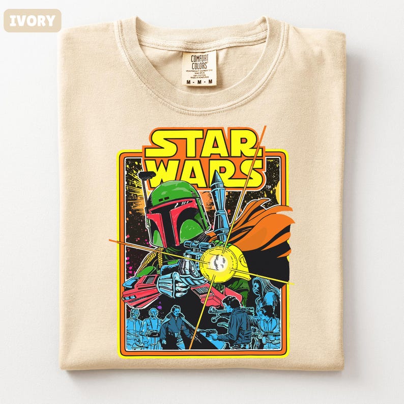 May include: Ivory-colored t-shirt featuring a Star Wars graphic. The design includes the text "STAR WARS" in yellow, with an image of Boba Fett and other characters. The shirt is a Comfort Colors brand, size M-M-M.