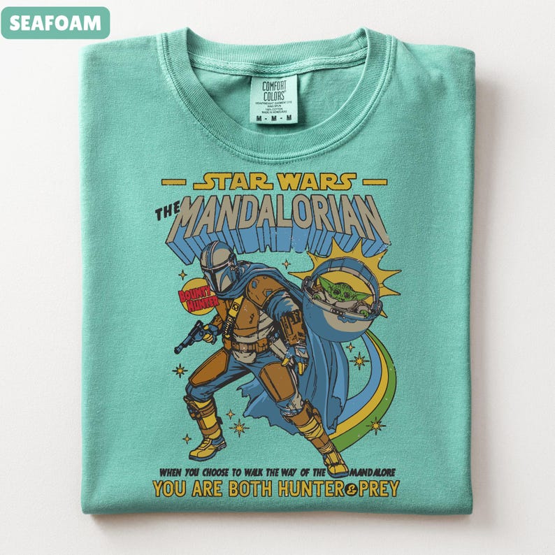 以下が含まれることがあります： スターウォーズのマンダロリアンをフィーチャーした、シーフォームグリーンのTシャツ。デザインにはマンダロリアン、グローグー、そして「When you choose to walk the way of the Mandalore, you are both hunter & prey.」というテキストが含まれています。
