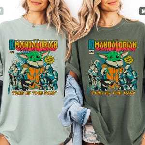 May include: Two t-shirts, one in bay and one in moss, featuring a comic book style graphic. The graphic includes the text "THE MANDALORIAN" and "THIS IS THE WAY", along with an illustration of Grogu and other characters.