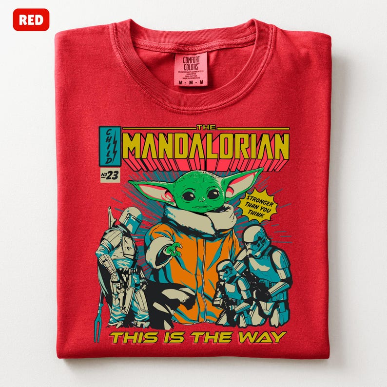 May include: Red t-shirt featuring a comic book style graphic of The Mandalorian. The graphic includes the Child, Stormtroopers, and the text "The Mandalorian", "Stronger Than You Think", and "This Is The Way". The shirt is a Comfort Colors brand.