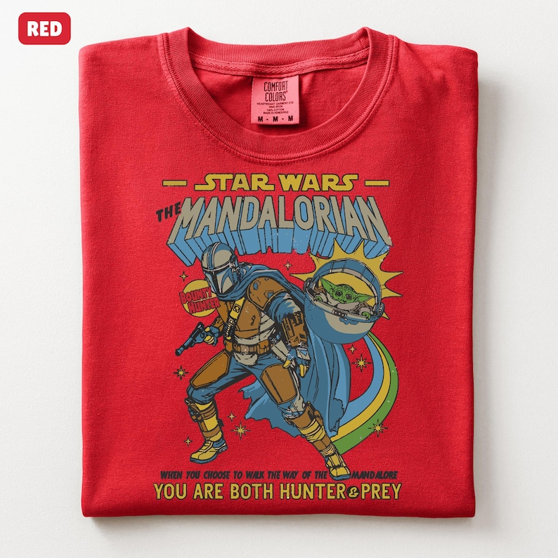 以下が含まれることがあります： スターウォーズのマンダロリアンのグラフィックが特徴の赤いTシャツ。デザインにはマンダロリアン、ベビーヨーダのようなキャラクター、そして「マンダロリアン」と「あなたはハンターと獲物の両方である」というテキストが含まれています。