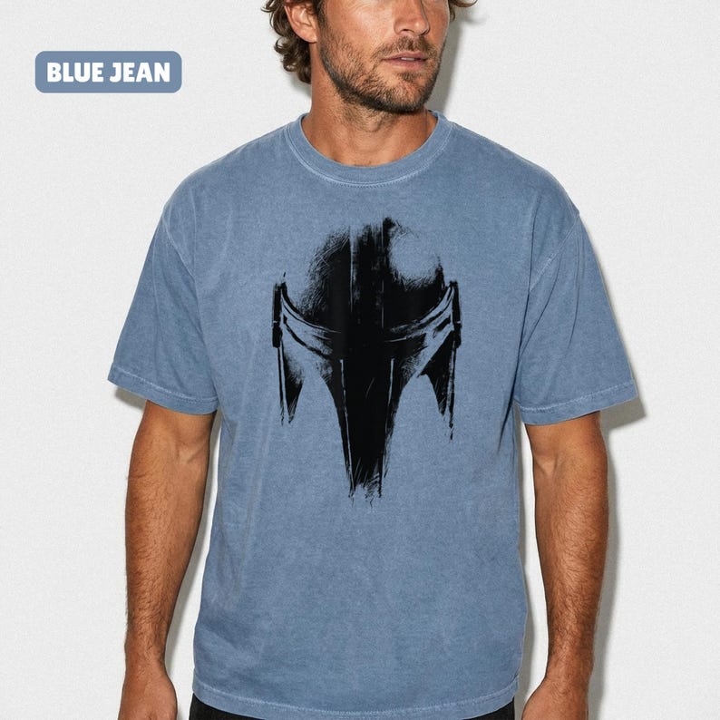 May include: Blue short-sleeved t-shirt featuring a black helmet graphic. The shirt has a faded look, with the text "BLUE JEAN" in a blue box in the top left corner.