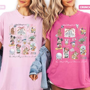 May include: Two t-shirts, one light pink and one fuchsia, featuring a colorful graphic design. The design includes various Disney characters and landmarks, with the text "Walt Disney World" and "2026". The phrase "The Most Magical Place on Earth" is also present.