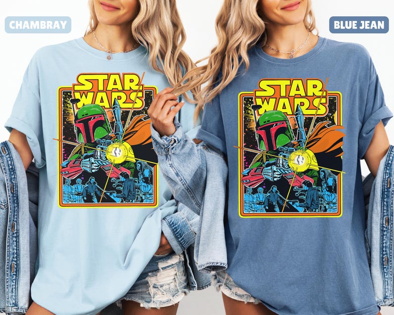 May include: Light blue and blue jean Star Wars graphic t-shirts. Each shirt features a colorful graphic of Boba Fett and other characters, with the Star Wars logo in yellow and orange. The shirts have short sleeves and a relaxed fit.
