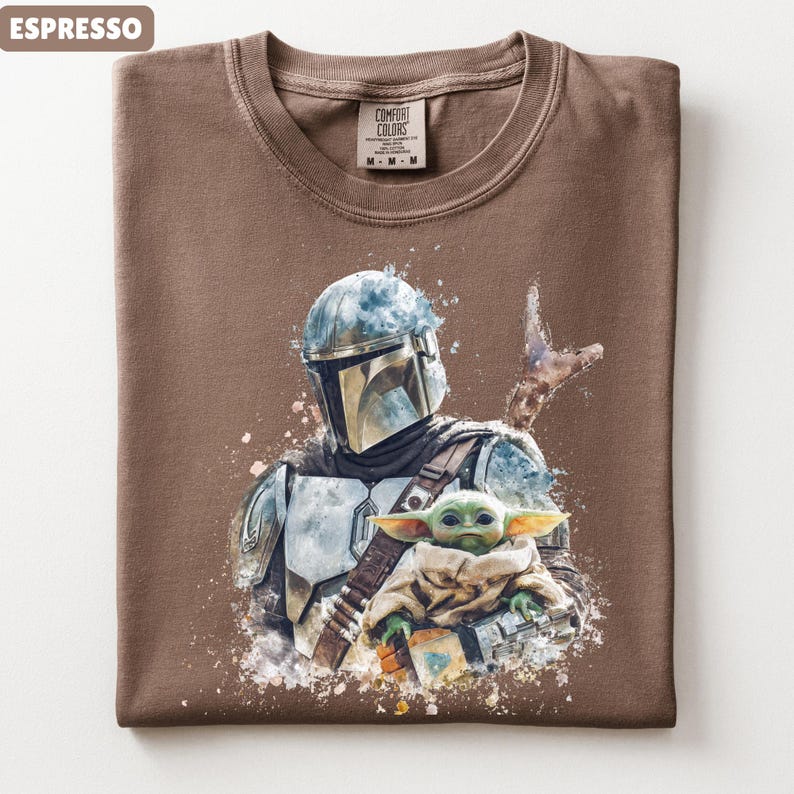 Puede incluir: Camiseta color espresso con una ilustraci&oacute;n estilo acuarela de The Mandalorian y Grogu. El dise&ntilde;o incluye el casco y la armadura del Mandaloriano, y Grogu envuelto en una manta. La camiseta tiene cuello redondo y una etiqueta Comfort Colors.