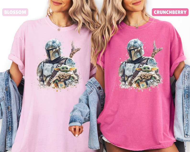 Puede incluir: Dos camisetas, una rosa claro y otra magenta, cada una con una ilustraci&oacute;n en acuarela de un personaje mandaloriano y Grogu. La camiseta rosa claro tiene la palabra "BLOSSOM" en un cuadro rosa. La camiseta magenta tiene la palabra "CRUNCHBERRY" en un cuadro rosa.