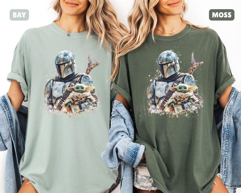 Puede incluir: Dos camisetas, una en color verde claro y otra en verde oscuro, cada una con una ilustraci&oacute;n al estilo acuarela. La ilustraci&oacute;n representa a un personaje con casco sosteniendo una peque&ntilde;a criatura verde. Las camisetas son informales y tienen las mangas dobladas.