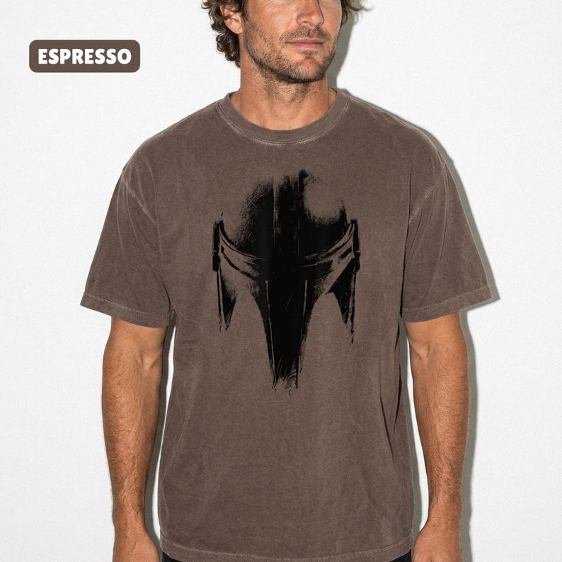 May include: Espresso-coloured t-shirt with a black helmet graphic. The short-sleeved shirt has a crew neck and a relaxed fit. The graphic is centered on the chest. The shirt is made of a soft, comfortable material.