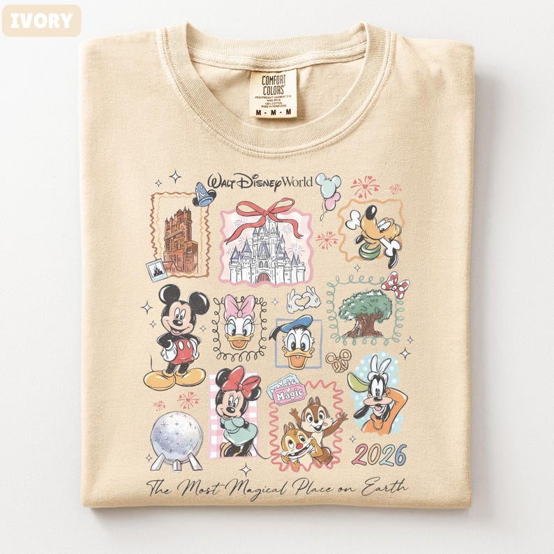 May include: Ivory-colored Comfort Colors t-shirt featuring a colorful graphic of Walt Disney World characters and landmarks. The design includes Mickey Mouse, Minnie Mouse, Donald Duck, and Goofy, along with the text "Walt Disney World" and "2026".