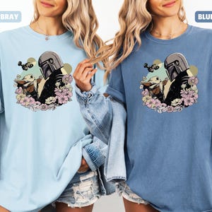 May include: Light blue and blue jean t-shirts featuring a graphic of a character in a helmet with a baby character surrounded by flowers. The text "CHAMBRAY" and "BLUE JEAN" are above the shirts.