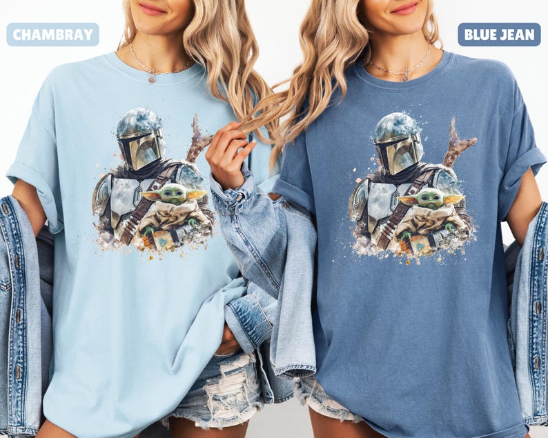 Puede incluir: Dos camisetas, una azul claro y otra azul, cada una con una ilustraci&oacute;n al estilo acuarela de The Mandalorian y Grogu. La camiseta azul claro est&aacute; etiquetada como "CHAMBRAY" y la azul como "BLUE JEAN".