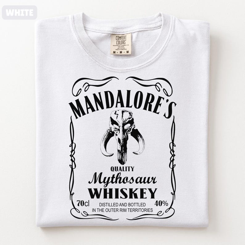 Puede incluir: Camiseta blanca con un dise&ntilde;o gr&aacute;fico negro. El dise&ntilde;o se asemeja a una etiqueta de whisky y presenta el texto "MANDALORE'S Mythosaur WHISKEY" junto con una imagen de calavera. La camiseta tambi&eacute;n incluye el texto "70cl" y "40%."