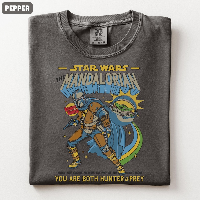 以下が含まれることがあります： スターウォーズのマンダロリアンが描かれた、ダークグレーのTシャツ。マンダロリアン、グローグー、そして「YOU ARE BOTH HUNTER & PREY」の文字がデザインされています。Comfort Colorsブランドのシャツです。