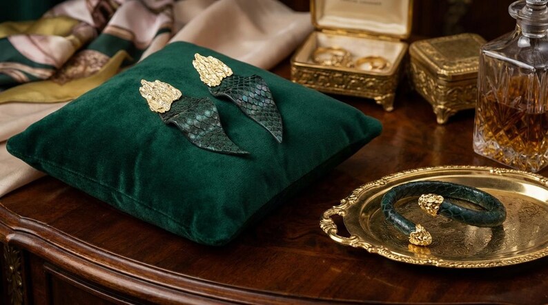 Puede incluir: Pendientes y pulsera con detalles dorados y un dise&ntilde;o de piel de serpiente verde. Los pendientes est&aacute;n sobre un coj&iacute;n de terciopelo verde. La pulsera est&aacute; en una bandeja dorada.