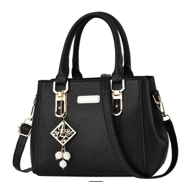 May include: Black handbag with top handles and a detachable shoulder strap. The bag features gold-tone hardware, a decorative charm, and a textured exterior. The bag has a rectangular shape with a structured design.
