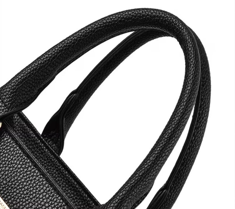 May include: Close-up of a black handbag with textured leather. The curved handles are thick and sturdy, designed for comfortable carrying. The bag's design suggests a classic, elegant style.