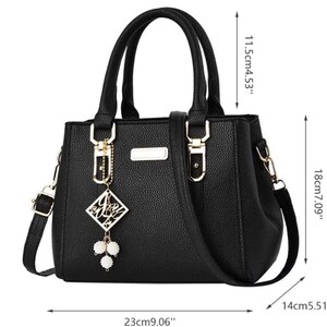 May include: Black handbag with top handles and a detachable shoulder strap. The bag features gold-tone hardware and a decorative charm. Dimensions: 9.06" long, 7.09" high, and 5.51" wide.