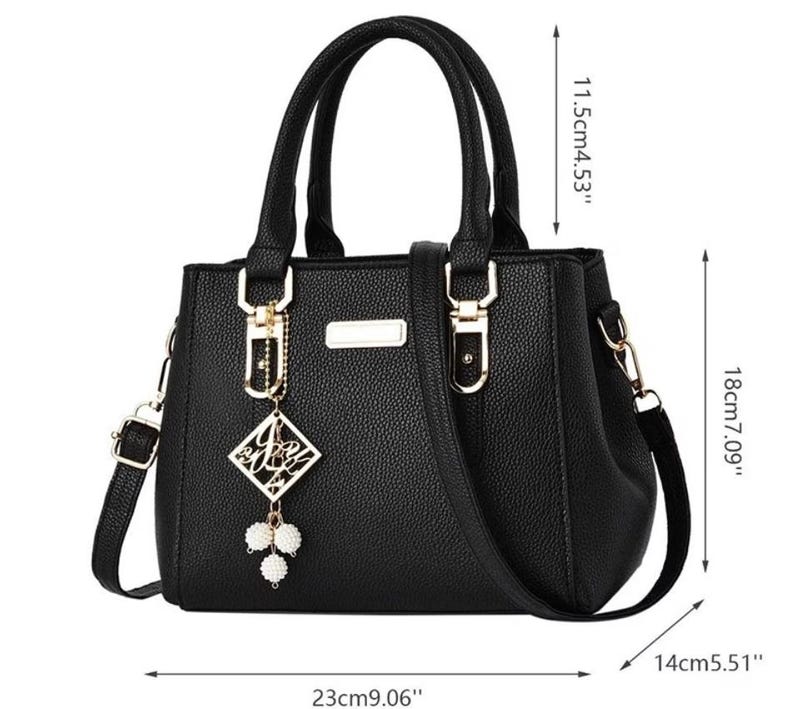 May include: Black handbag with top handles and a detachable shoulder strap. The bag features gold-tone hardware and a decorative charm. Dimensions: 9.06" long, 7.09" high, and 5.51" wide.