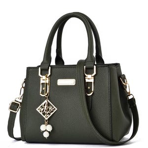 May include: Dark green handbag with top handles and a detachable shoulder strap. The bag features gold-colored hardware, including clasps and a decorative charm with white pearl accents. The bag has a textured surface and a rectangular shape.