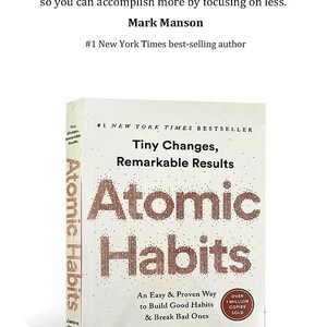 Peut inclure: Livre &agrave; couverture rigide intitul&eacute; "Atomic Habits" de James Clear. La couverture est blanche avec le titre en grandes lettres marron pix&eacute;lis&eacute;es. Le livre promet un moyen facile de cr&eacute;er de bonnes habitudes et d'en briser de mauvaises.