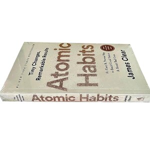 Peut inclure: Un livre intitul&eacute; "Atomic Habits" de James Clear. La couverture blanche porte le titre en grandes lettres marron pointill&eacute;es. Le sous-titre est "Tiny Changes, Remarkable Results". Le livre est emball&eacute; sous film plastique.