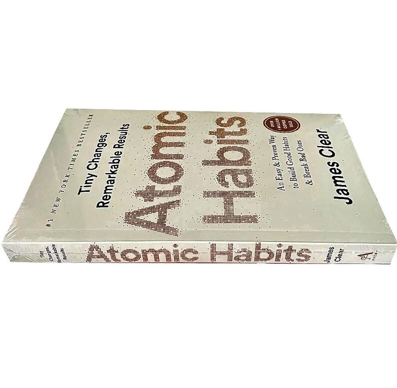 Peut inclure: Un livre intitul&eacute; "Atomic Habits" de James Clear. La couverture blanche porte le titre en grandes lettres marron pointill&eacute;es. Le sous-titre est "Tiny Changes, Remarkable Results". Le livre est emball&eacute; sous film plastique.