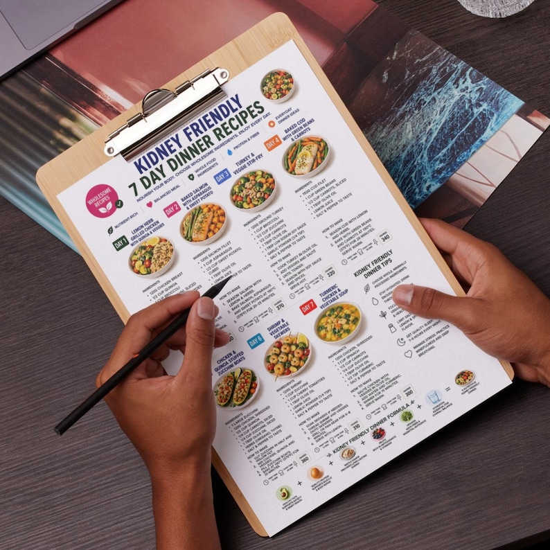 May include: A wooden clipboard holding a printed document titled Kidney Friendly 7 Day Dinner Recipes. The page features a structured meal plan with daily food illustrations, ingredient lists, and cooking instructions for seven distinct dinner meals.