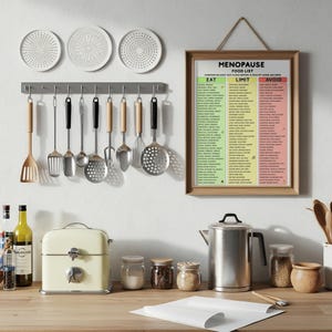 May include: A kitchen scene with various utensils hanging above a countertop. Includes a cream-colored toaster, a stainless steel kettle, and a framed "Menopause Food List" poster. Several jars with lids and a wooden cutting board are also visible.