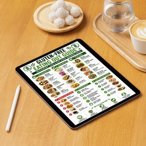 K&ouml;nnte beinhalten: Ein Tablet mit einem "Gluten-Free Eating Out Guide" mit verschiedenen Essensoptionen. Das Tablet liegt auf einem Holztisch, zusammen mit einem wei&szlig;en Stift, Kokosb&auml;llchen und Kaffee. Ein Glas Wasser ist ebenfalls zu sehen.