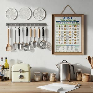 Puede incluir: Una pared de cocina con un cuadro enmarcado del plan de comidas GLP-1 7 Day Meal Plan, un soporte gris con utensilios de metal y madera, tres platos decorativos blancos, una panera color crema, una tetera de metal y frascos de vidrio.