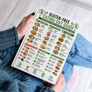 K&ouml;nnte beinhalten: Eine Person h&auml;lt einen wei&szlig;-gr&uuml;nen "Gluten-Free Eating Out Guide" mit Ideen f&uuml;r Bestellungen in Restaurants, Caf&eacute;s und Fast-Food-Restaurants. Der Leitfaden enth&auml;lt Essensoptionen, Tipps und h&auml;ufige Gluten-Ausl&ouml;ser. Der Leitfaden wird &uuml;ber dem Scho&szlig; einer Person gehalten.
