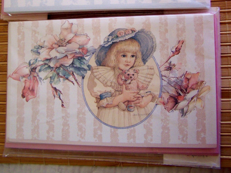 Pode incluir: Uma menina com cabelo loiro e um chap&eacute;u rosa e azul segura um urso de peluche. Ela est&aacute; cercada por flores rosa e brancas. O fundo &eacute; um padr&atilde;o listrado rosa e branco.
