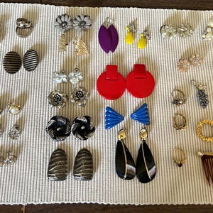 May include: A large collection of vintage earrings, including clip-on earrings, dangle earrings, and stud earrings. The earrings are made from a variety of materials, including metal, plastic, and glass. The earrings are in a range of colours, including gold, silver, black, white, red, blue, and green.