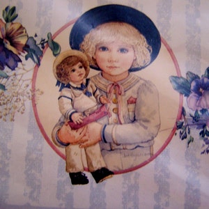Pode incluir: Uma ilustra&ccedil;&atilde;o vintage de uma menina vestindo um traje de marinheiro azul e um chap&eacute;u preto segurando uma boneca com um vestido branco e um colar de marinheiro azul. A ilustra&ccedil;&atilde;o &eacute; cercada por um c&iacute;rculo rosa e detalhes florais.
