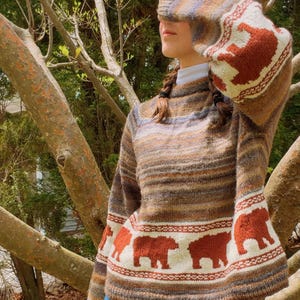 May include: A long-sleeve knit sweater featuring a horizontal striped pattern in shades of brown, tan, and blue. The sweater includes a white band near the hem and cuffs decorated with a repeating pattern of rust-colored bear silhouettes.